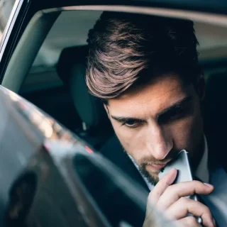 Ein Mann mit ernster Miene blickt auf sein Telefon, während er auf dem Rücksitz eines Autos sitzt und die Customer Journey für sein B2B-Unternehmen analysiert.